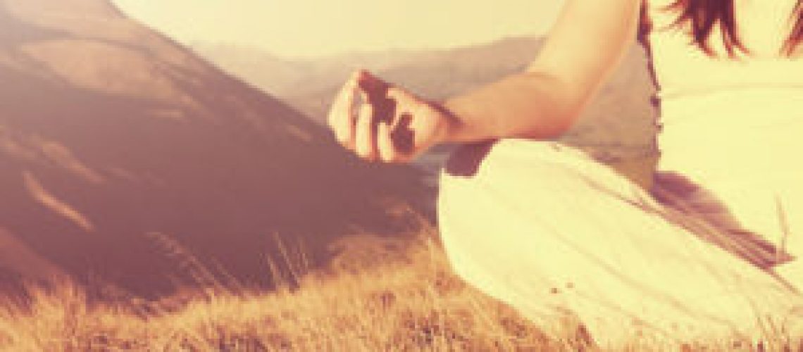 Lady meditating in lotus position on top of the mountain.