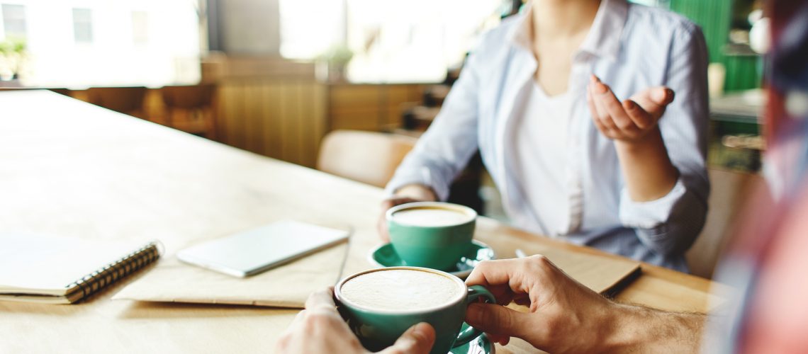 Faceless shot of chilling friends drinking delicious coffee and chatting while sitting with studies at table