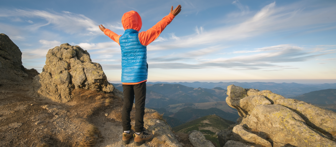 young-child-boy-hiker-standing-with-raised-hands-mountains-enjoying-view-amazing-mountain-landscape-sunset